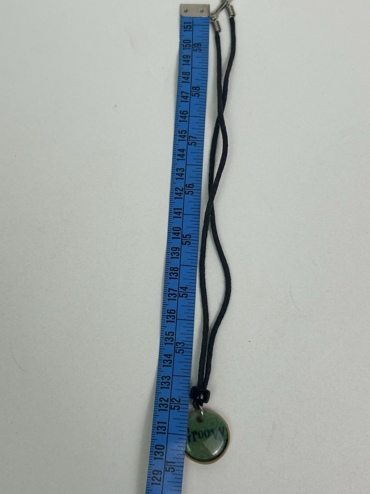 Vintage black cord necklace features a green pendant with “Groovy” inscribed