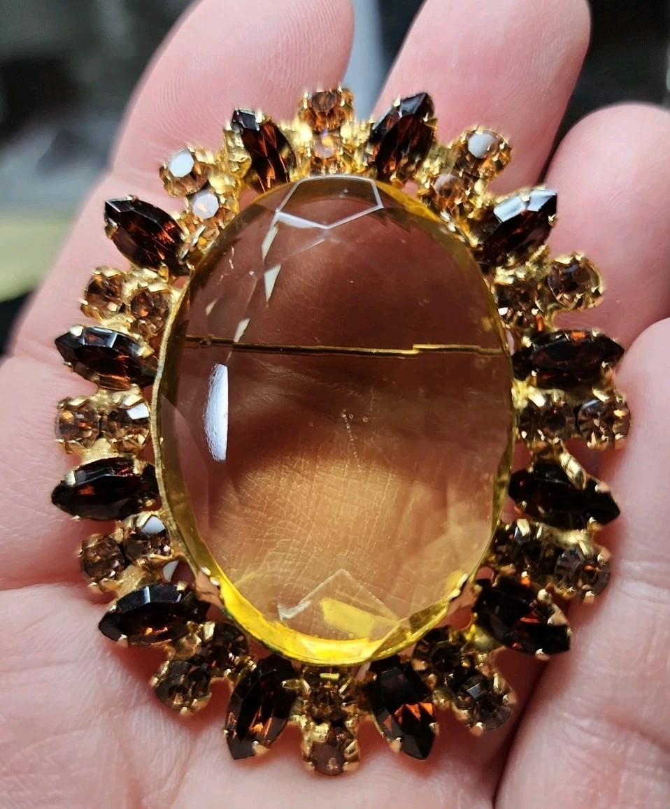 A vintage gold-tone brooch featuring a large, faceted yellow central stone.