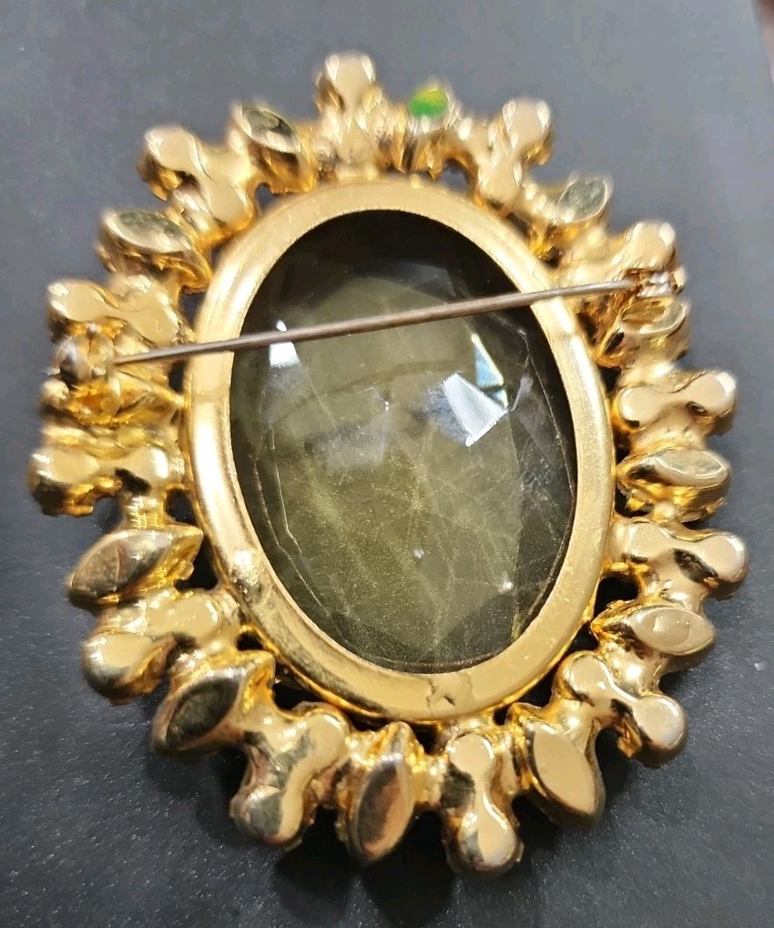 A vintage gold-tone brooch featuring a large, faceted yellow central stone.