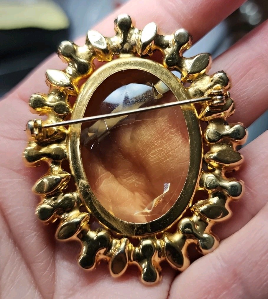 A vintage gold-tone brooch featuring a large, faceted yellow central stone.