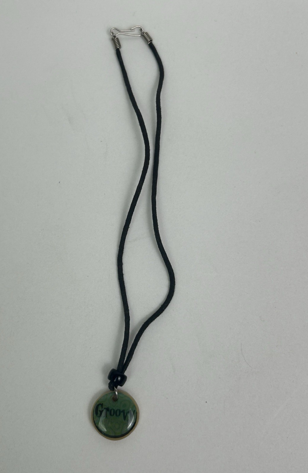 Vintage black cord necklace features a green pendant with “Groovy” inscribed