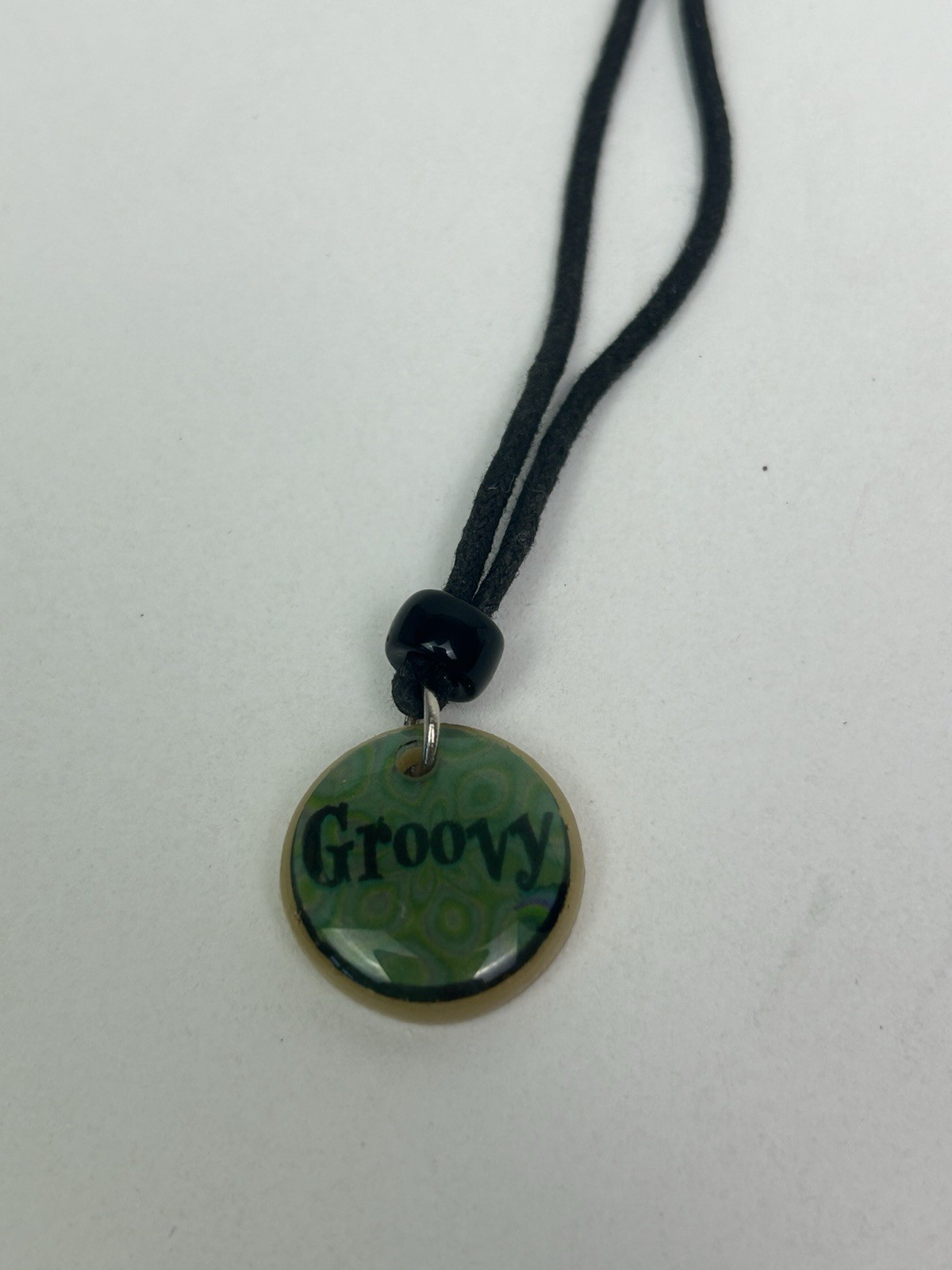 Vintage black cord necklace features a green pendant with “Groovy” inscribed